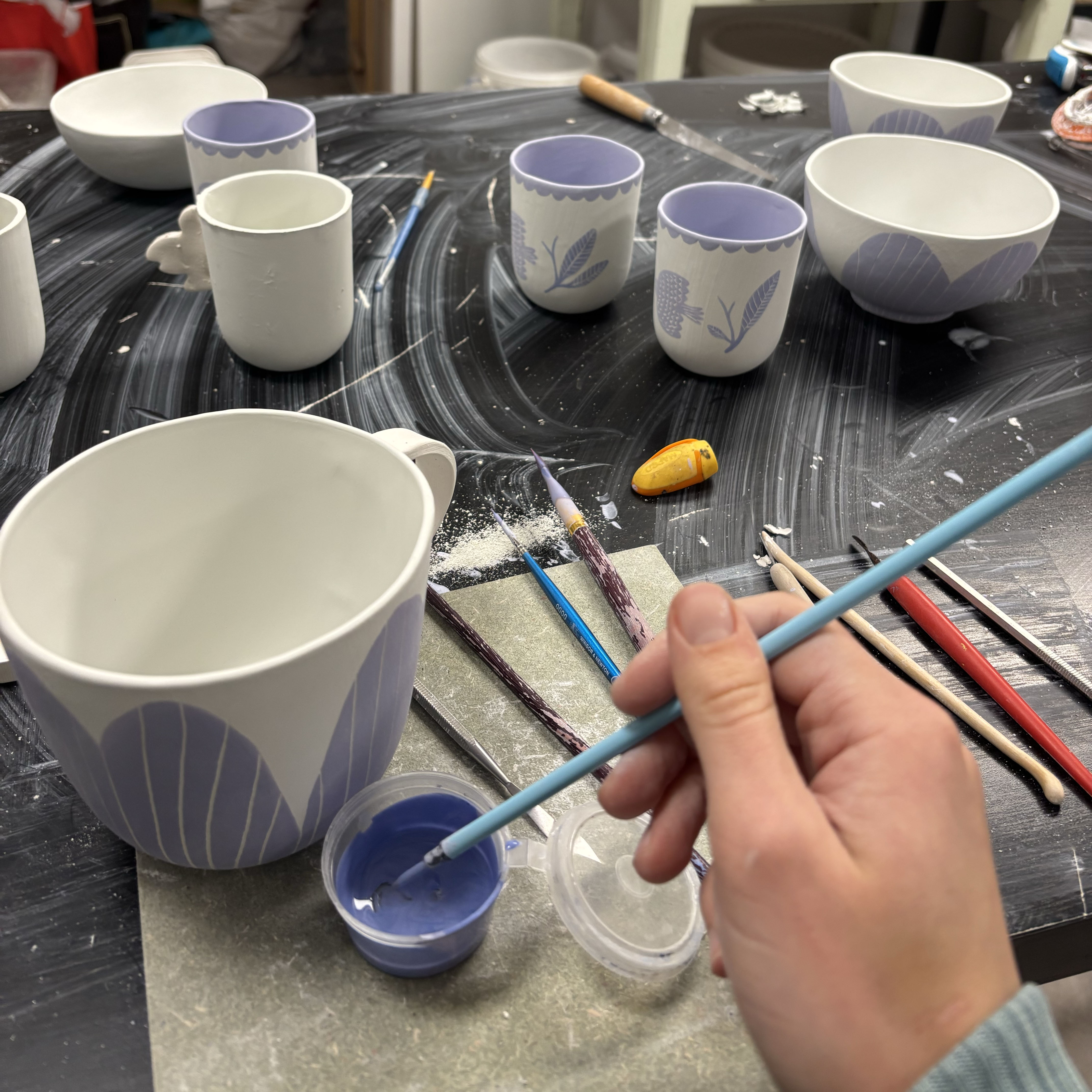 main qui tien in pinceau, plusieurs pièce crue entrain d’être peintes en violet