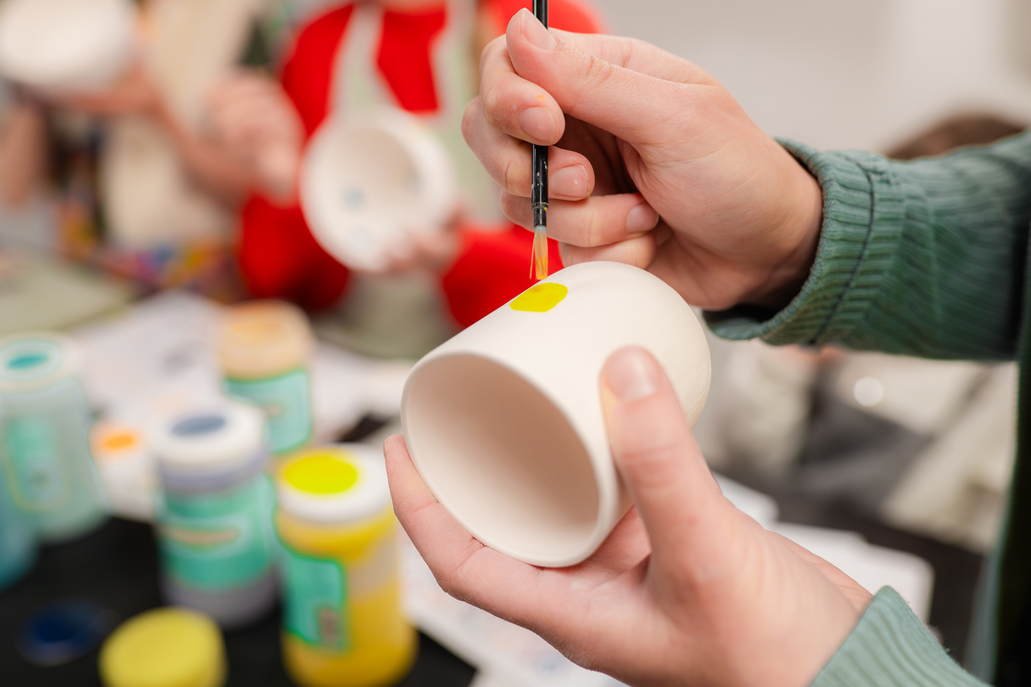 photo de deux main entrain de peindre une tasse en porcelaine avec de l'engobe jaune